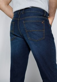 Jeans in denim blu scuro con taglio dritto, dotati di due tasche posteriori con cuciture a contrasto e una texture liscia.