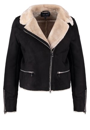 Kvinde iført sort lammeskindjakke, lyserød bluse, sorte skinny bukser, sorte ankelstøvler, der holder sort håndtaske med nitter.