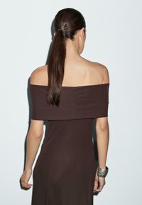 Robe marron à épaules dénudées avec une silhouette ajustée, une texture lisse et un design midi, complétée par un bracelet manchette en argent.