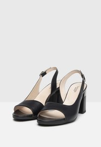 Tacchi slingback in pelle nera con punta aperta, fascia larga sulla parte anteriore e tacco a blocco. Cinturino alla caviglia regolabile per una vestibilità ottimale.