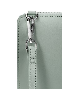 Light green leather handbag corner featuring a silver zipper pull and a detachable strap with reinforced stitching and a metal attachment loop.