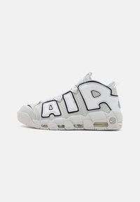 Witte sportieve sneakers met grote zwarte "AIR" letters. Bevatten mesh- en leermaterialen, gestructureerde accenten en zichtbare luchtkussens.