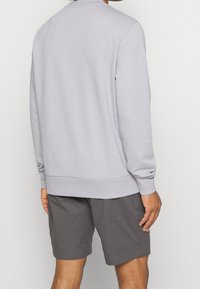 Ljusgrå sweatshirt med långa ärmar och ribbade muddar, kombinerad med mörkgrå shorts. Slätt tyg med avslappnad passform. Enfärgad design.