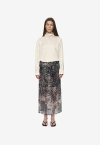 Haut à manches longues en crème douce associé à une jupe pailletée longue en sequins gris foncé. Des sandales noires viennent compléter la tenue.