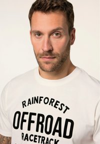 White cotton t-shirt featuring bold black text "RAINFOREST OFFROAD RACETRACK." Short sleeves and a crew neckline. Smooth texture.
