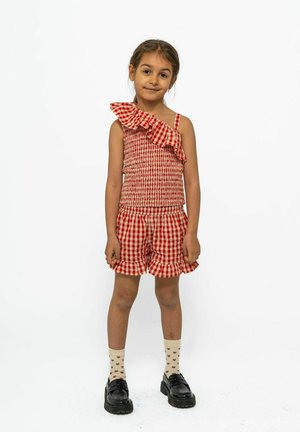 Rood en wit geruite tweedelige outfit met een off-shoulder top met ruches en bijpassende shorts, gecombineerd met zwarte schoenen en gestreepte sokken.