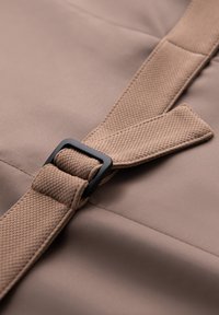 Gros plan d'une sangle en tissu beige texturé passant à travers une boucle rectangulaire noire sur un textile beige lisse.