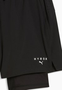 Shorts de sport noirs avec texte blanc "HYROX" et logo Puma près de l'ourlet, avec une poche latérale et une partie supérieure ventilée.