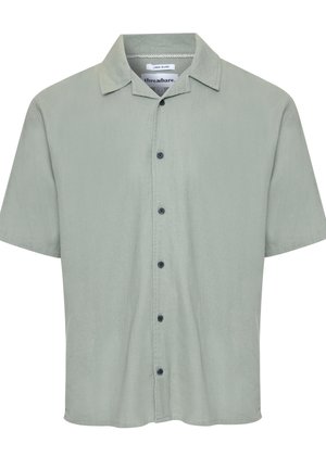 Chemise à manches courtes en lin vert clair avec un devant à boutons et un col évasé. Présente six boutons foncés et un ourlet droit.