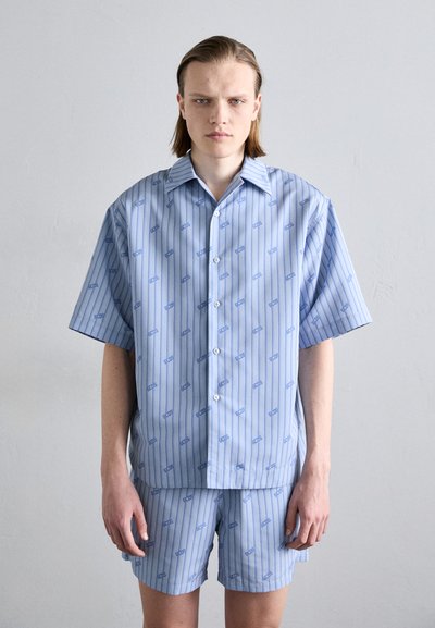 Light blue short-sleeve shirt and matching shorts, featuring vertical stripes and repeating text pattern. Material appears smooth and lightweight.