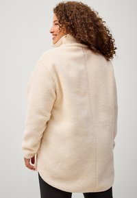 Giacca in pile color crema con colletto alto, superficie testurizzata, maniche lunghe e vestibilità rilassata, caratterizzata da un sottile dettaglio di cucitura sul retro.