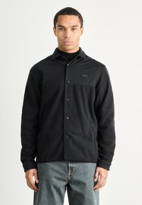 Casaco de fleece preto com fecho à frente por botões, colarinho espalhado e bolso no peito. Apresenta um tecido texturizado e bolsos laterais.