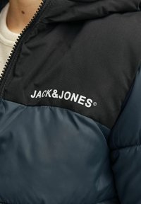 Puffīgs nepiepildīts mētelis ar melnu augšējo daļu un tumši zilu apakšējo daļu. Iekļauj rāvējslēdzēju un baltu logo "JACK&JONES" uz krūtīm.