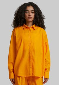 Bright orange long-sleeve shirt with a button-down collar, featuring a relaxed fit and smooth texture, with front button closure and classic cuffs.
