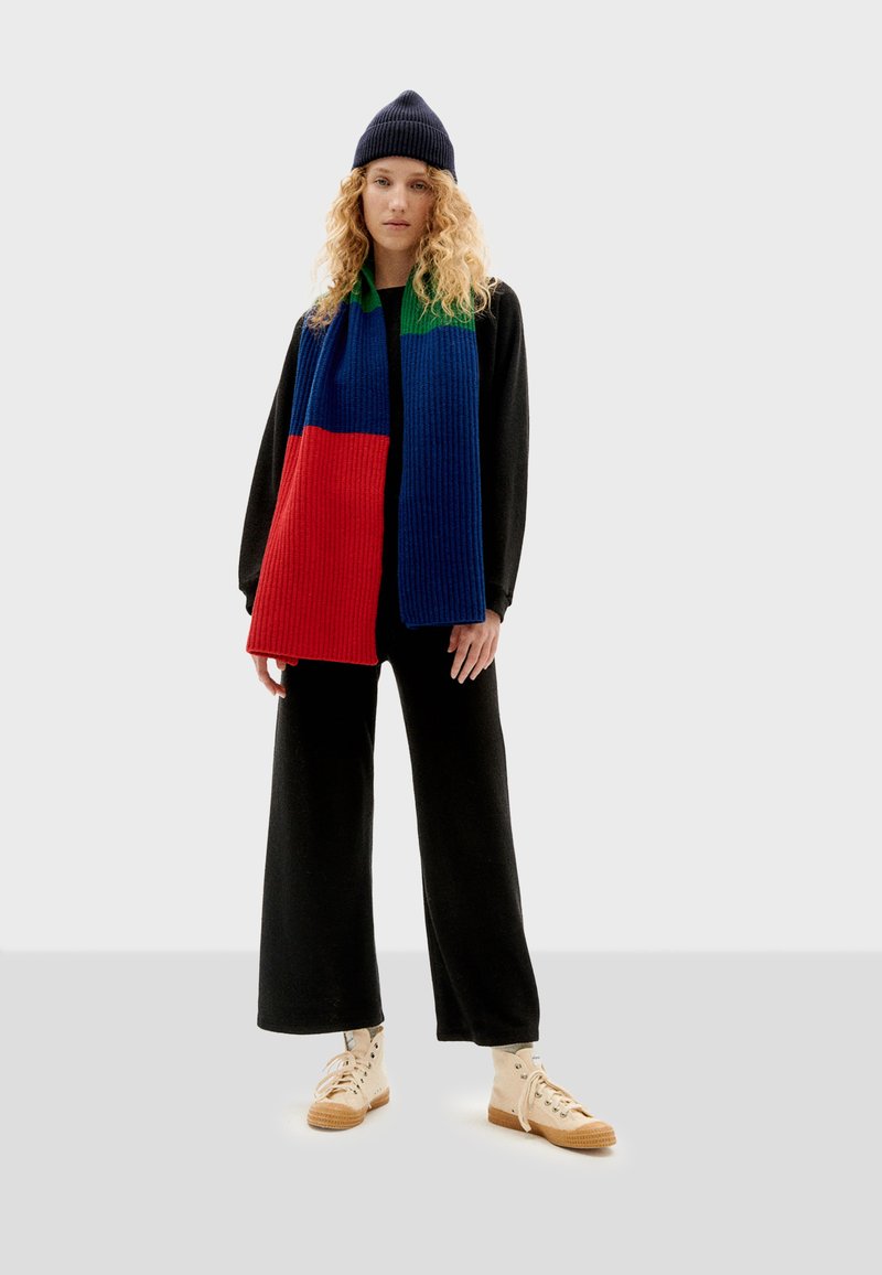 Czarne spodnie szerokie, czarna bluzka z długim rękawem, żywy prążkowany szalik w czerwonych, niebieskich i zielonych odcieniach oraz granatowa dzianinowa czapka. Buty w kolorze ecru.