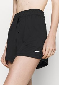 Pantalones cortos deportivos negros con cintura elástica y cordón, que presentan un logotipo blanco de Nike en el dobladillo inferior y aberturas laterales para mayor movilidad.