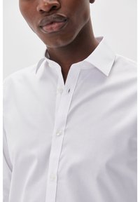 Witte katoenen shirt met een klassieke kraag, knoopsluiting aan de voorkant en een enkele knoopdetail. De stof lijkt glad en lichtgewicht te zijn.