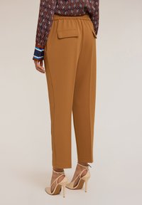 Pantaloni marroni a sigaretta con vita elasticizzata, due tasche posteriori e cuciture laterali; abbinati a décolleté con cinturino alla caviglia beige.