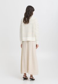 Pull crème avec des rayures beige clair, design court, manches longues, associé à une longue jupe maxi beige fluide et des sandales à talons noires.