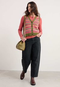 Zeleni pleteni prsluk s višebojnim uzorkom, preko ružičaste majice dugih rukava. Crne široke hlače i smeđe čizme do gležnja upotpunjuju odjevnu kombinaciju.