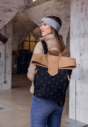 Black and white polka dot backpack with brown suede flap and handle, featuring adjustable straps and minimalistic design.