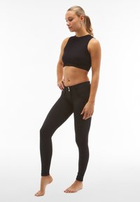 Top corto a coste nero abbinato a leggings neri a vita alta con una texture liscia e due bottoni frontali per la chiusura.