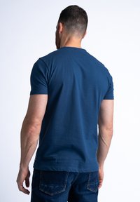Mørkeblå bomulds t-shirt med korte ærmer og rund halsudskæring, vist fra ryggen. Glat tekstur med minimal udsmykning.