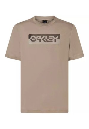 T-shirt beige à manches courtes Oakley avec un logo rectangulaire comportant des lignes ondulées et le nom de la marque sur la poitrine.
