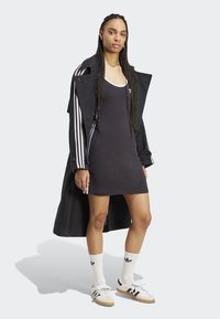 Čierne šaty s vrstvou pod dlhým čiernym kabátom s bielymi pruhmi na rukávoch. Bielé ponožky s čiernym logom a športové topánky dopĺňajú celý outfit.