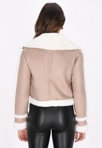 Lichtbruine faux suede jas met een witte fleece kraag en manchetten. Kort ontwerp, gladde textuur en zichtbare stiksels.