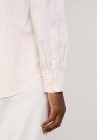 Camisa de botones con un patrón de cuadros en rosa y blanco, de manga larga y puños abotonados. Fabricada con tela tejida de textura suave.