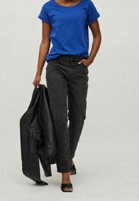 Modré tričko s krátkým rukávem, černé džíny s vysokým pasem a černé sandály na podpatku. Nosí černou koženou bundu na rameni.