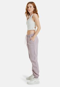 Witte geribde crop top met uitsnijdingen, gecombineerd met licht lila joggers met een elastische taille en zijzakken, gedragen met witte sneakers.