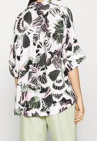 Blouse fluide à manches courtes blanche avec un imprimé papillon vif en noir, vert et rose. Tissu léger avec une coupe décontractée.