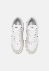 Baskets blanches avec une tige lisse en synthétique, des accents en daim, des détails perforés, des lacets plats et une semelle extérieure en caoutchouc. Logo sur la languette.