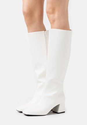 Weiße knielange Stiefel mit einer glatten Synthetikleder-Oberfläche, quadratischen Zehen und Blockabsätzen. Verfügt über einen seitlichen Reißverschluss für einfaches An- und Ausziehen.