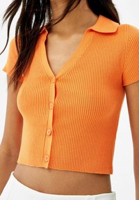 Cardigan corto in maglia a coste di un vivace arancione, con scollo a V e maniche corte, dotato di cinque bottoni coordinati lungo il davanti.