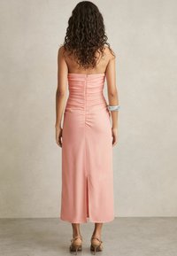 Rosa strapless satin klänning med rynkdetaljer, knähög slits bak, och en slät textur. Har en enkel design och en figursydd silhuett.