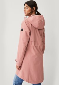 Abrigo impermeable de color rosa claro con capucha, detalles de botones y una abertura en la parte posterior. Presenta mangas largas y un corte relajado, adecuado para el uso casual.