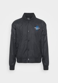 Blouson bomber noir à boutons pression avec col, poignets et ourlet côtelés, arborant un petit logo des Brooklyn Nets bleu et blanc sur la poitrine gauche.