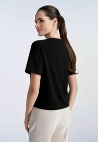 Czarny t-shirt z krótkim rękawem i okrągłym dekoltem, gładka tekstura oraz luźny fason, połączony z jasnymi spodniami.