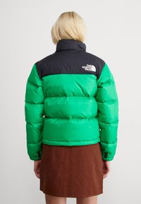 Zelena i crna puffer jakna s visokim ovratnikom, s kvadratnim dizajnom i logotipom na gornjem dijelu leđa. Tekstuirana tkanina.