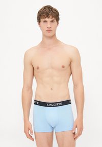 Svetlo modri bokserice s črnim pasom, na katerem je logo "LACOSTE". Mehka tkanina z udobnim prileganjem, minimalistična zasnova in brez vzorcev.