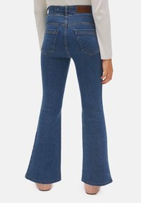 Vaqueros de campana de alta cintura en denim azul medio con una textura suave, bolsillos traseros y un parche de cuero de la marca en la cintura.