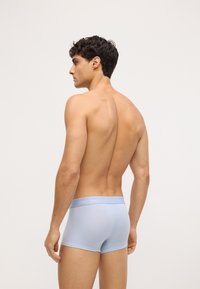 Boxeri scurți din bumbac de culoare albastră deschisă, cu un brâu moale ce prezintă logo-ul Calvin Klein, afișați din lateral pe un model. Textură netedă.