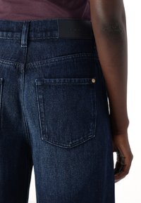 Mørkeblå denim jeans med høj talje, læderbæltepatch og to baglommer med diskret syning og guldfarvet hardware.