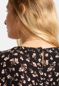 Vestido negro con flores pequeñas en tonos púrpura y rosa. Presenta un detalle en forma de llave en la parte de atrás, tejido texturizado y un delicado borde en forma de ola.