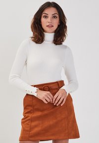 Hvid ribbet turtleneck sweater med lange ærmer og knaplukning ved manchetterne, parret med en brun suedeminiskørt med en stor bæltespænde.