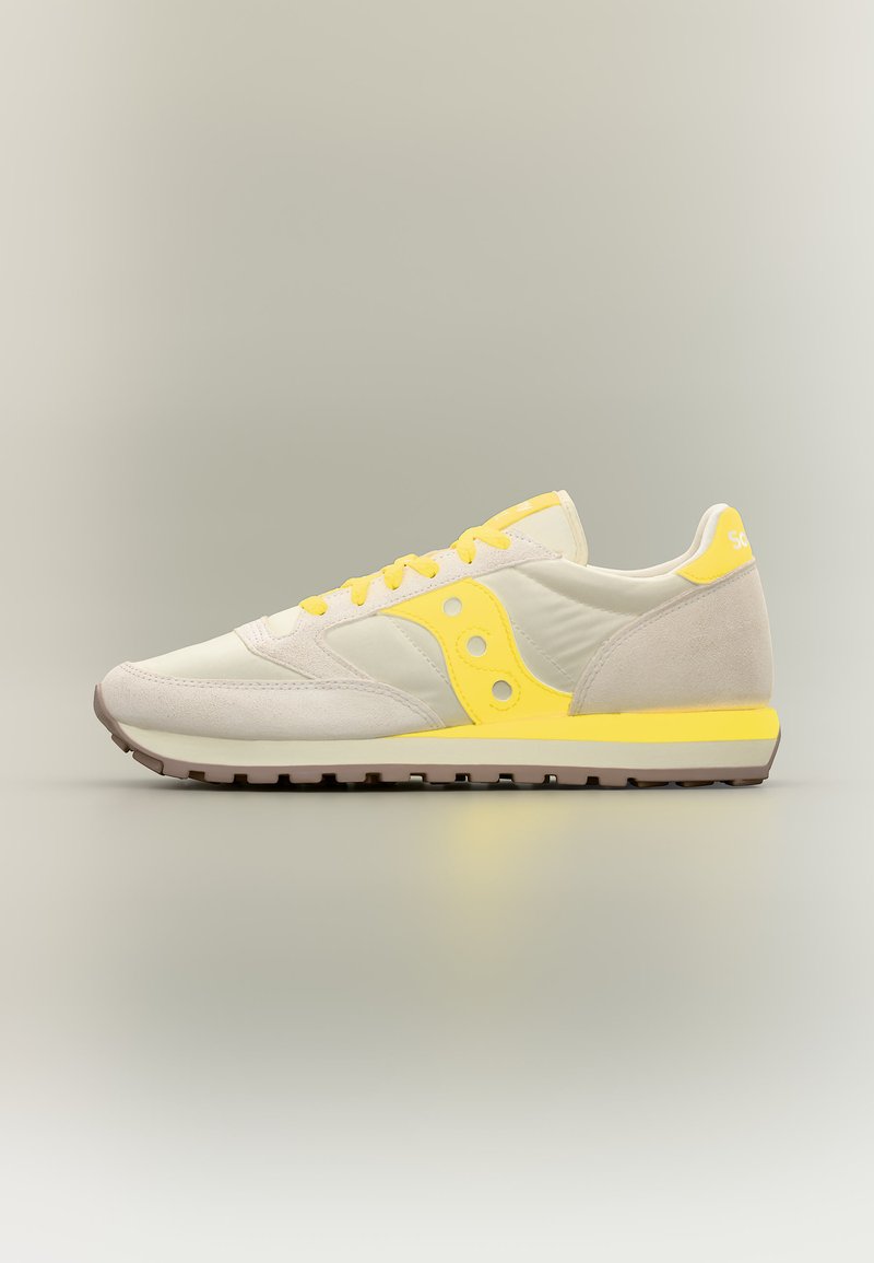 Μπέζ και κίτρινο χαμηλό sneaker με σουέντ λεπτομέρειες, κίτρινα κορδόνια και υφασμένο καφέ πέλμα, εμφανίζεται σε προφίλ σε ουδέτερο φόντο.