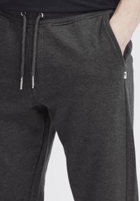 Donkergrijze joggingbroek van zacht materiaal, met een verstelbare tailleband met zilverkleurige metalen uiteinden en zijzakken.